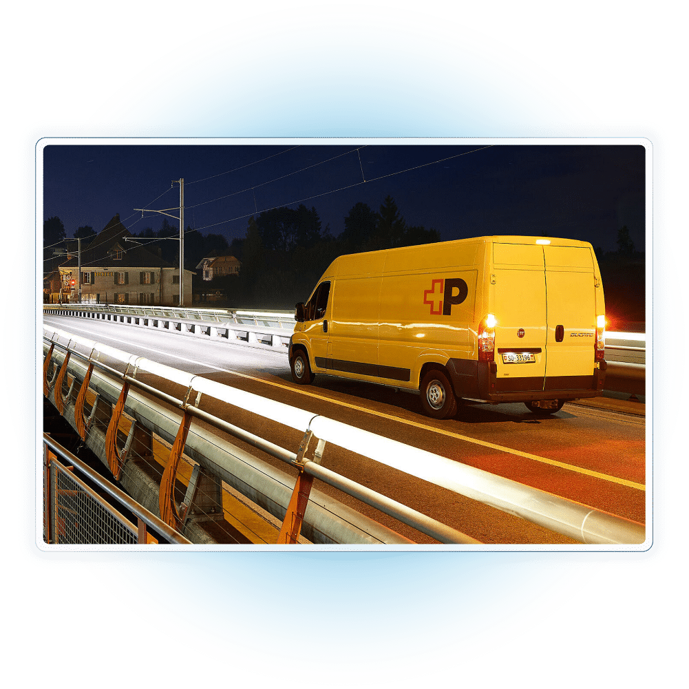 Gelbes Lieferfahrzeug eines Schweizer Paketdienstes bei der Last-Mile-Zustellung auf einer Brücke in der Dämmerung